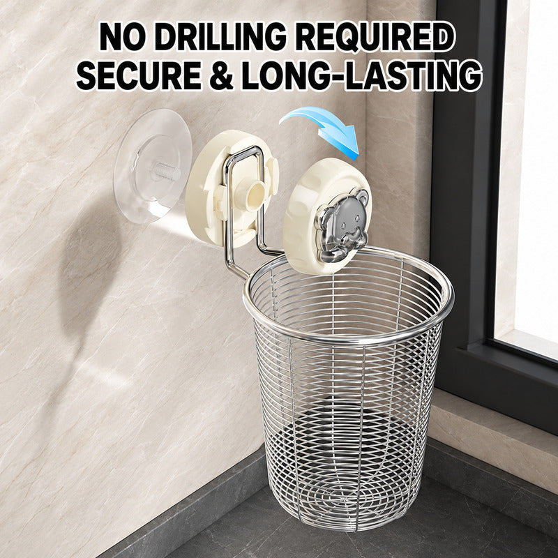 A stainless steel wire trash basket hanging from a wall-mounted suction cup holder, shown in a bathroom-like setting with a tiled wall and window frame. Large text at the top reads 'NO DRILLING REQUIRED SECURE & LONG-LASTING' with a blue arrow indicating the holder.