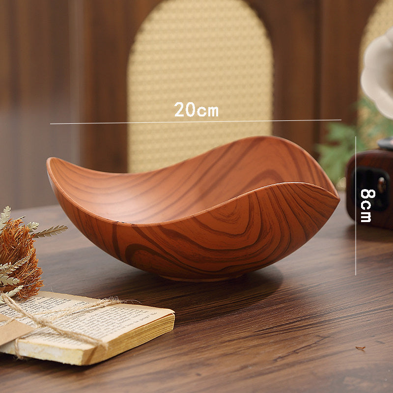 A curved wooden bowl with a rich brown wood grain pattern sits on a dark wooden table. White dimension lines overlay the image showing measurements of 20cm in width and 8cm in depth, with a blurred woven chair in the background.