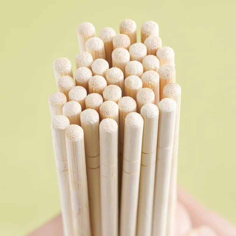 A close-up of a bundle of light natural wood chopsticks held in a hand against a pale yellow-green background.