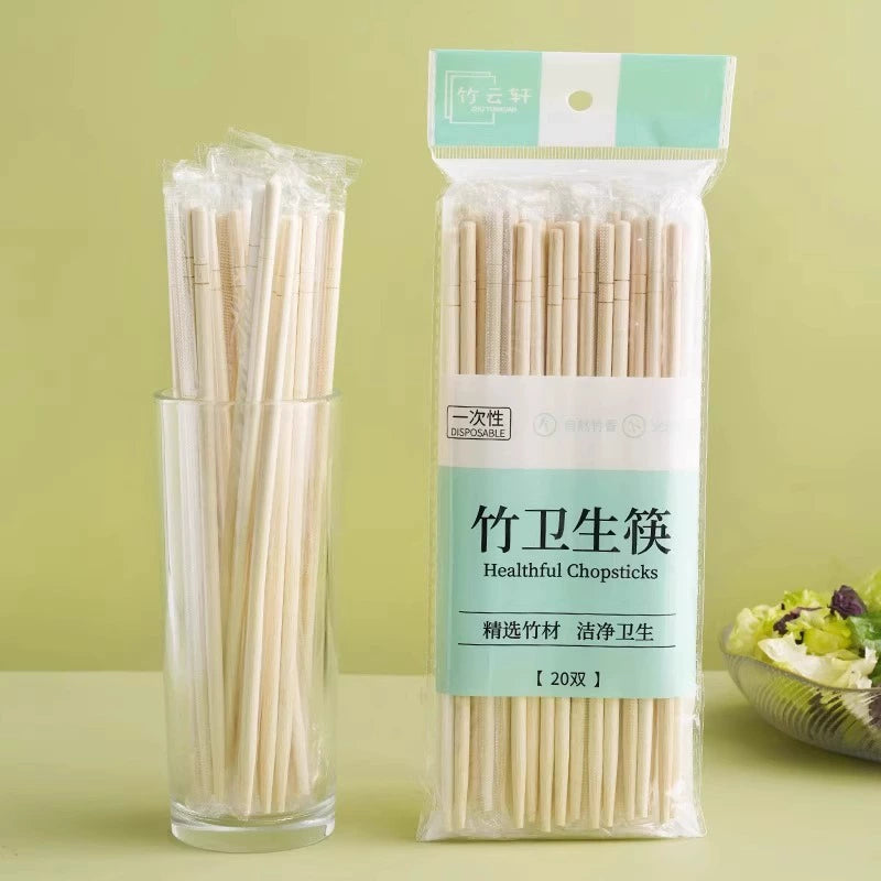 Pack of 20 bamboo chopsticks shown standing in a clear glass cup next to their retail packaging, on a light green background.