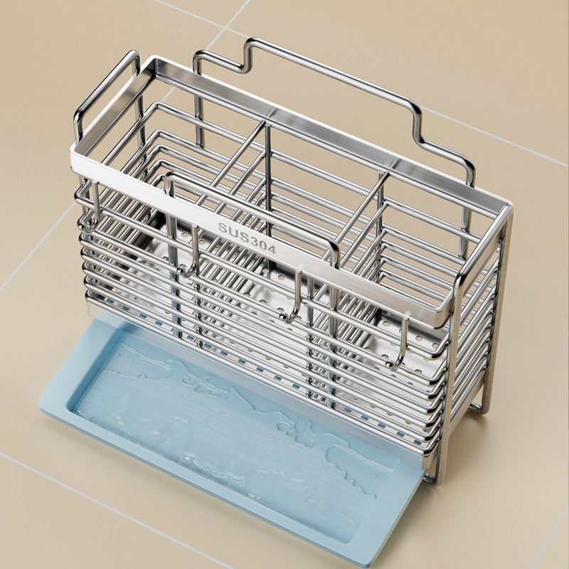 A stainless steel kitchen utensil holder with a handle and multiple compartments, shown stacked on top of a light blue silicone dish rack insert on a beige tiled background.