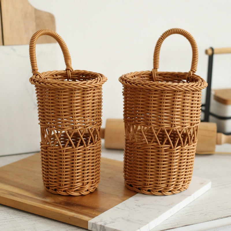 Two small woven wicker baskets with loop handles, shown side by side on a wooden board in a kitchen setting.