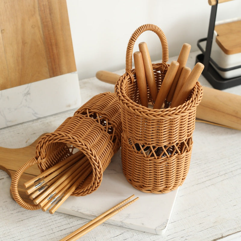 Two woven wicker chopstick holders on a white marble board, filled with wooden chopsticks, in a bright kitchen setting.