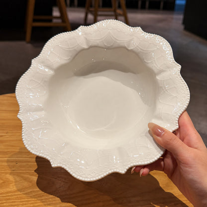 A white ceramic bowl with a decorative scalloped rim, held by a hand over a wooden table.