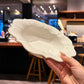 A hand holding a white ceramic bowl with an ornate, scalloped beaded rim in a blurred bar or cafe setting.