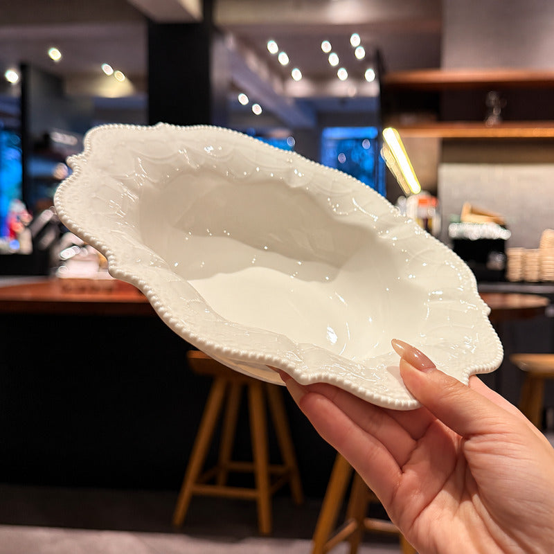A hand holding a white ceramic bowl with an ornate, scalloped beaded rim in a blurred bar or cafe setting.