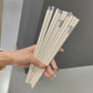 A hand holding a bundle of light beige chopsticks with silver metal tips, set against a modern gray and white background.