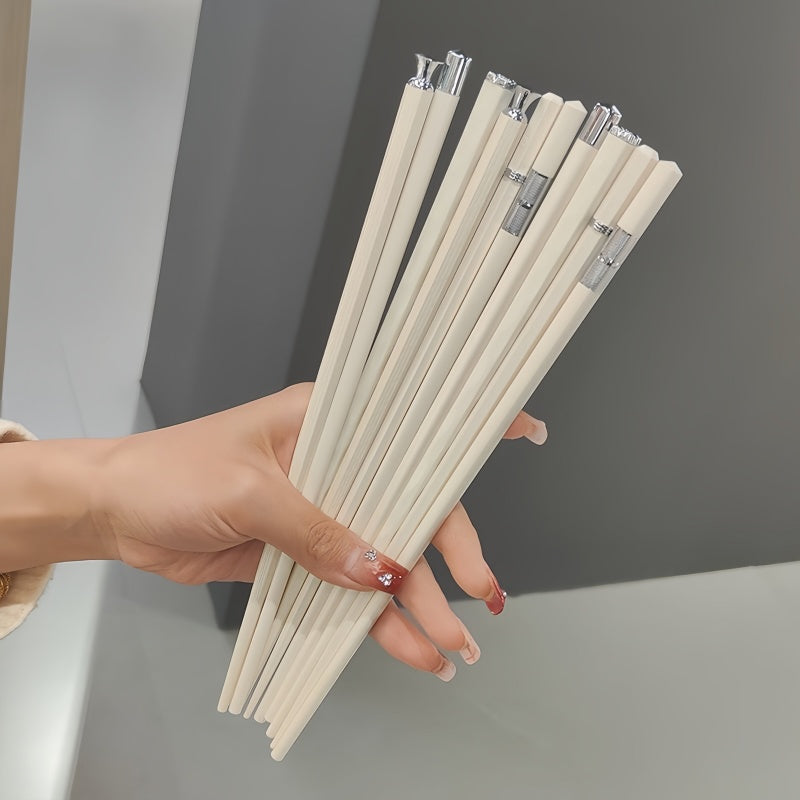 A hand holding a bundle of light beige chopsticks with silver metal tips, set against a modern gray and white background.